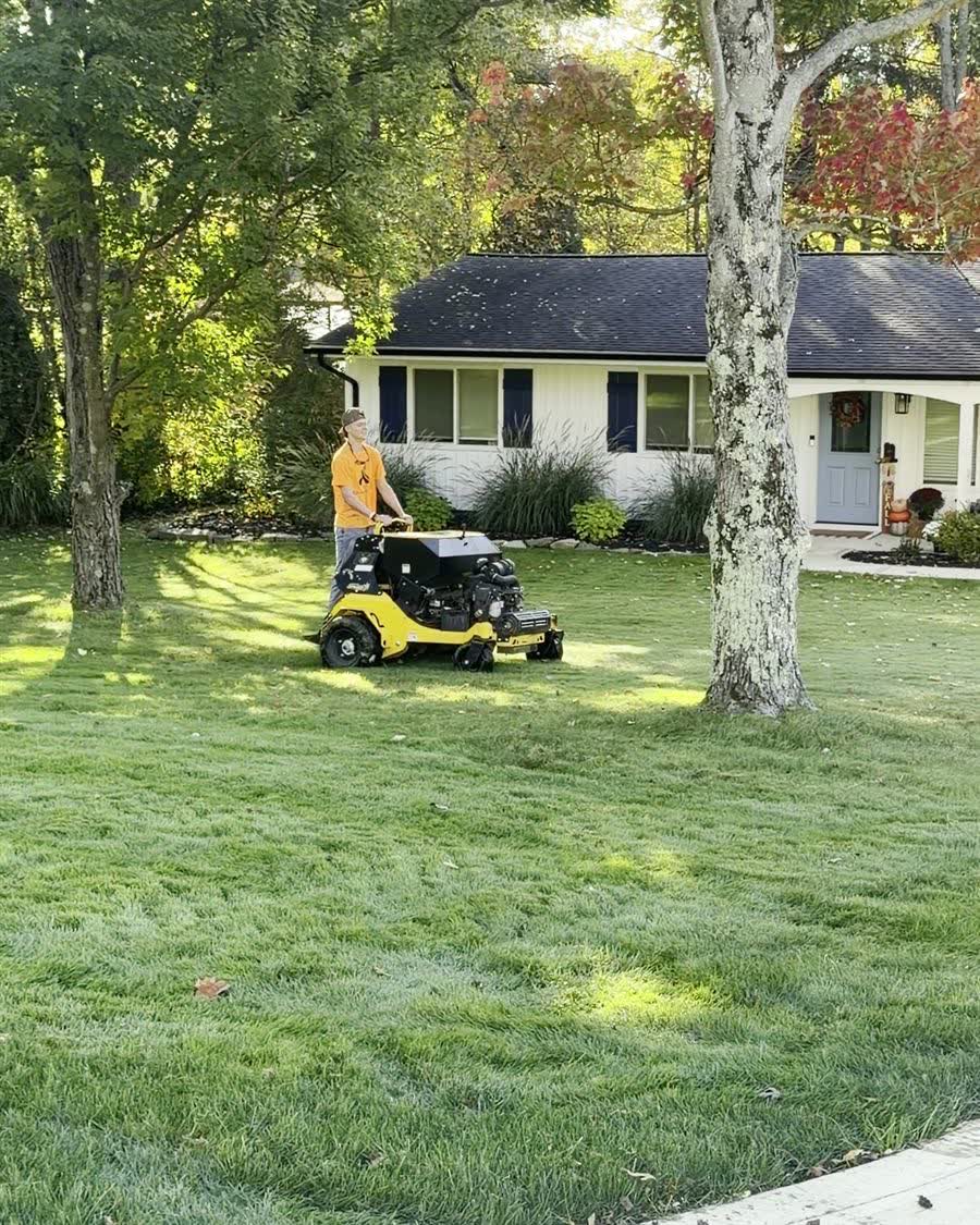Logan running the stand-on aerator across a front lawn