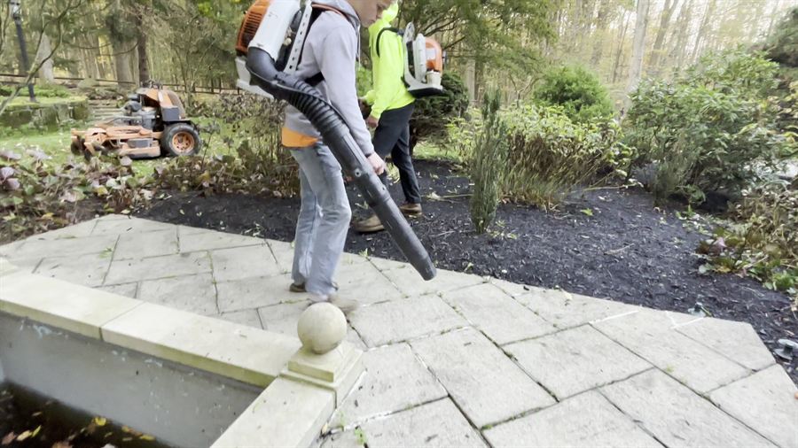 Two crew blowing leaves off a stone patio and out of the beds