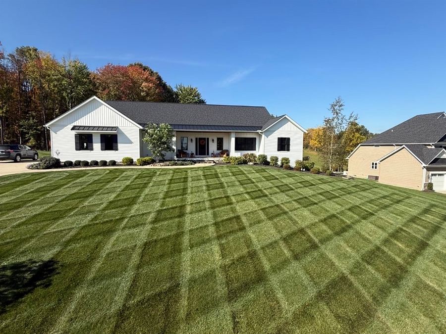 Crisscross mowing stripes across a big front lawn up to a white farmhouse